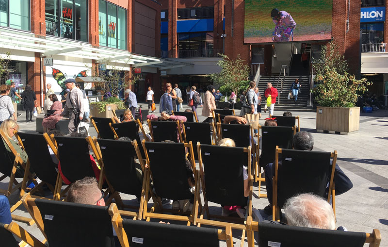 People on deckchairs watching sport on a big screen at the local Mall